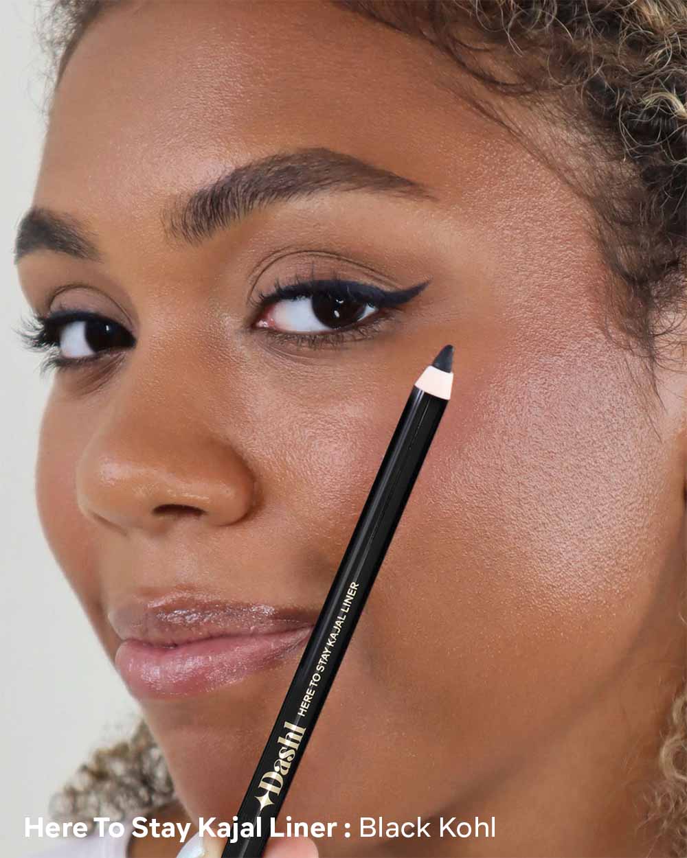 Woman applying Kajal eyeliner with a pencil, close-up of face and product.